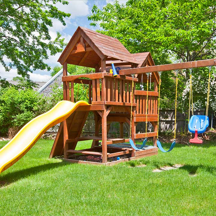 Spielturm aus Holz mit gelber Rutsche und Schaukeln im Garten